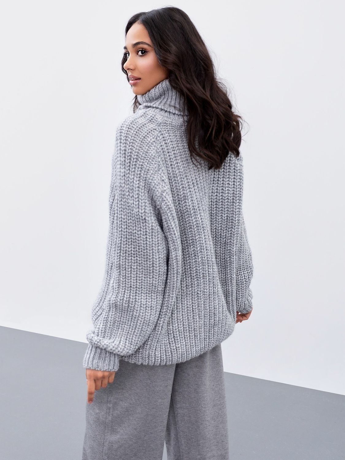 Об'ємний в'язаний светр з горлом сірого кольору - фото